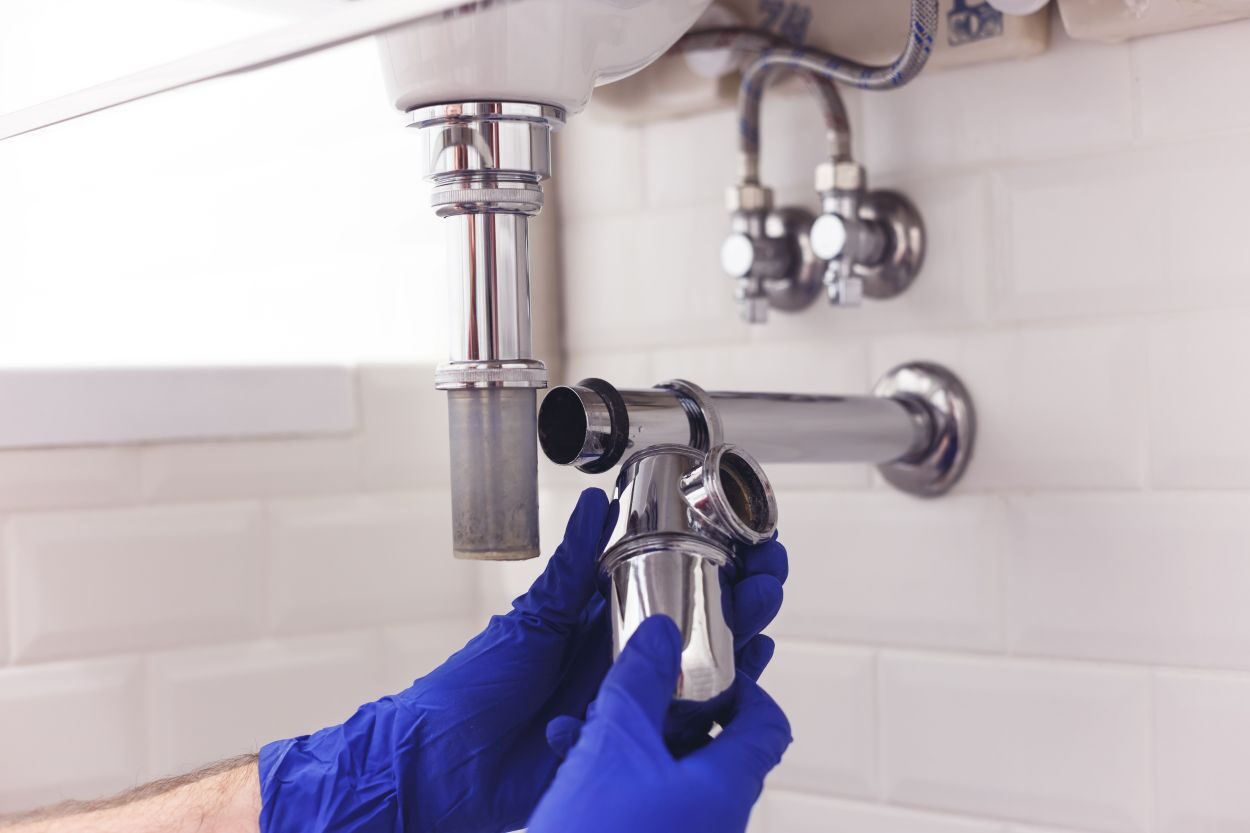 Plumber repairs and maintains chrome siphon under the washbasin. Plumber at work in bathroom, plumbing assemble and install concept